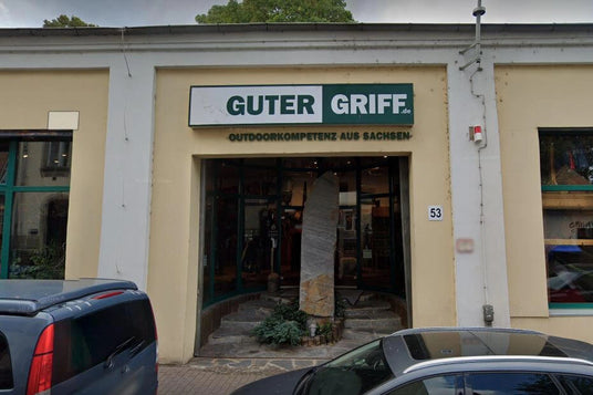 Foto des Eingangs vom Outdoor-Fachgeschäft 'Guter Griff' in Sachsen mit Schildern und Autos davor.