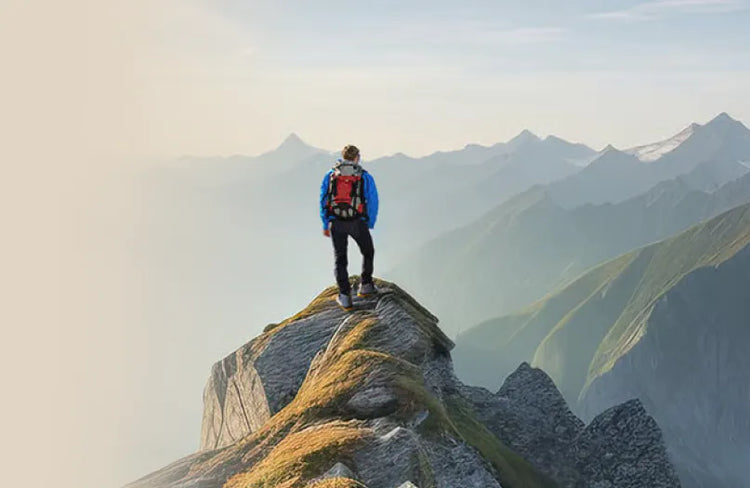 Person auf Bergkamm mit robustem Wanderstiefel, umgeben von Bergen und blauem Himmel. Text: Feel Free